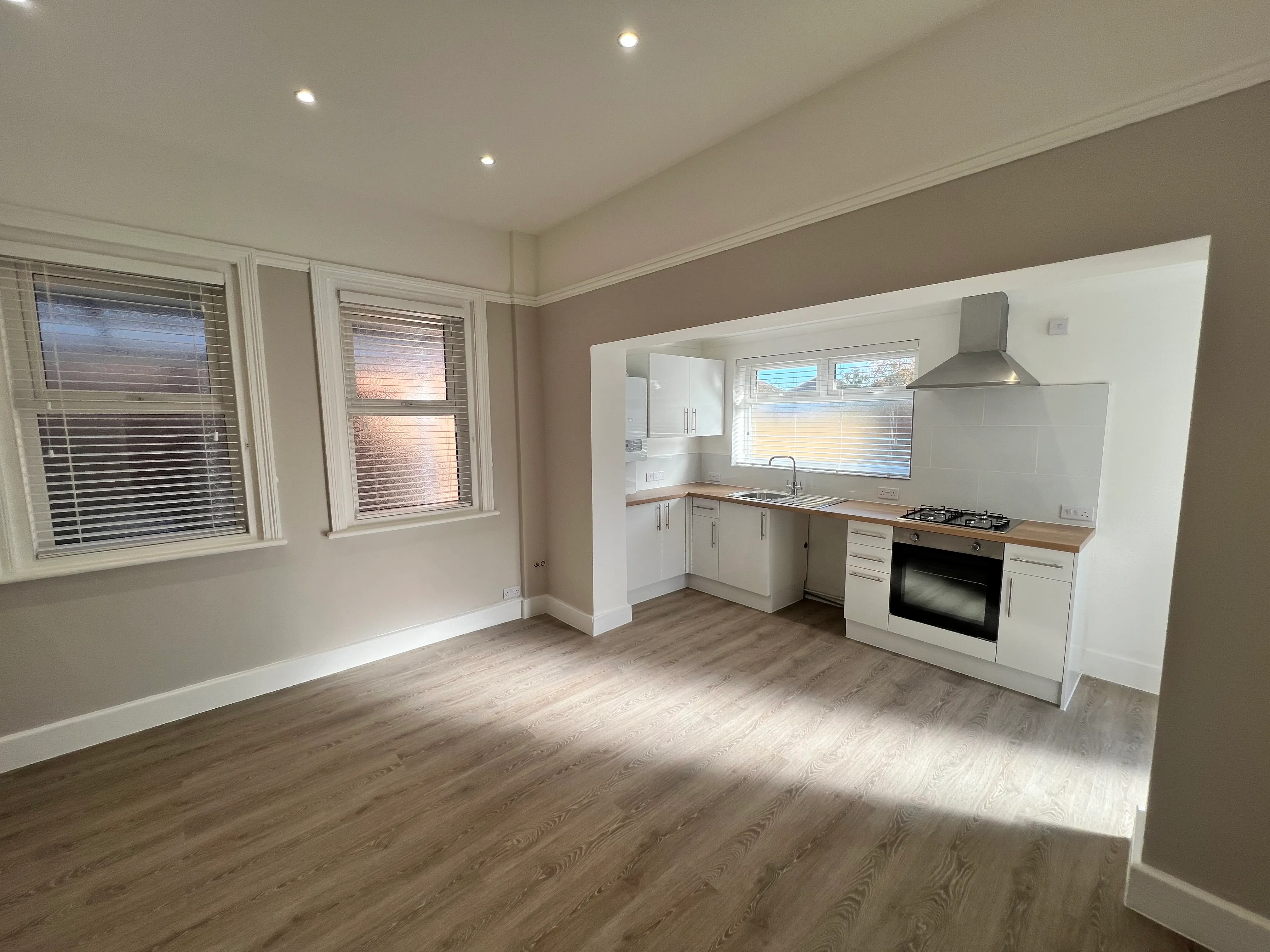 A finished flat: open-plan living room and white kitchen with a grey wood floor